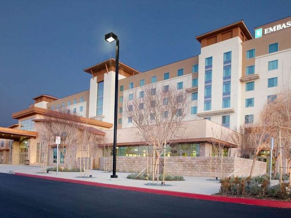 The image shows an Embassy Suites hotel building with several floors, exterior lights, an American flag, and sparse landscaping in front.