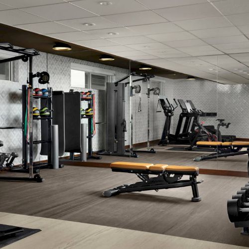 The image shows a gym with exercise equipment like treadmills, weight benches, and dumbbells, with mirrors on the walls.