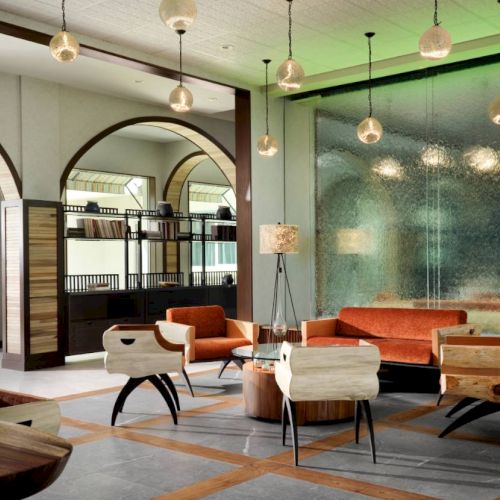 A modern lounge features stylish furniture, arched windows, pendant lights, and a textured glass wall, creating an inviting atmosphere.