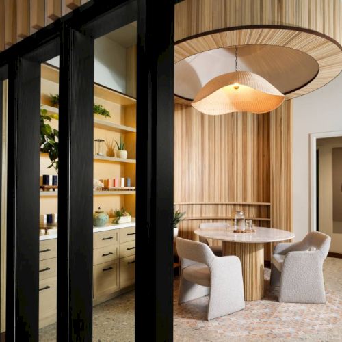 A modern dining area features a round table with upholstered chairs, wooden accents, and a unique overhead light fixture ending the sentence.