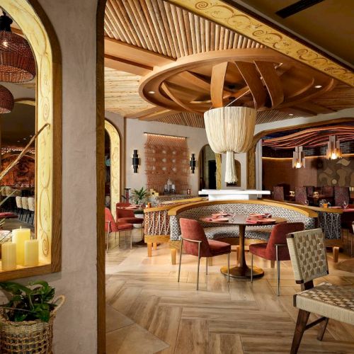 The image depicts a stylish, modern interior of a restaurant with wooden elements, decorative lighting, and elegantly set dining tables.