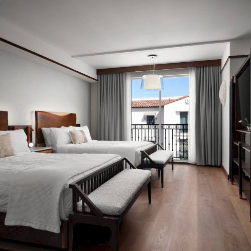 The image shows a modern hotel room with two beds, a window, and elegant decor, featuring natural light and wooden furnishings.