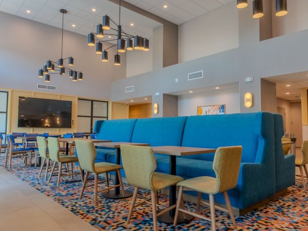 A modern lounge area with blue seating, yellow chairs, colorful rug, and large overhead lights in a spacious, well-lit room.