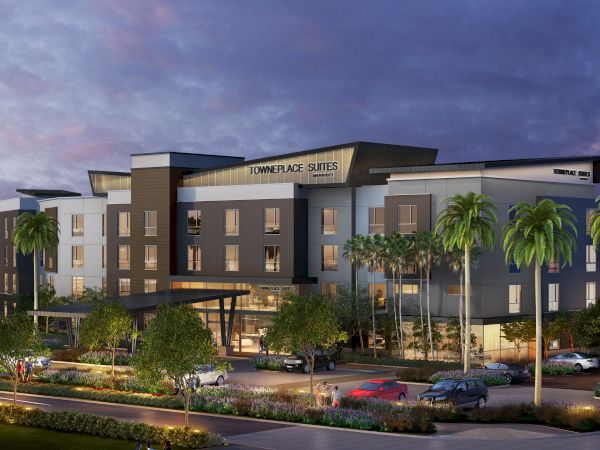 The image shows a modern hotel building at dusk, surrounded by palm trees and parked cars, with a sign reading "TownePlace Suites" on the facade.