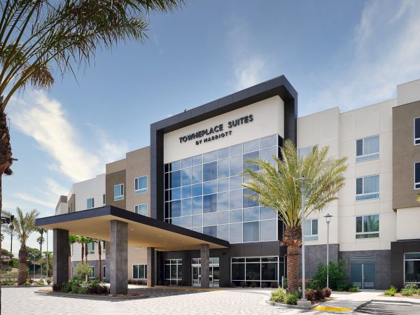 The image shows the exterior of a TownePlace Suites hotel by Marriott, with a contemporary design and palm trees nearby.