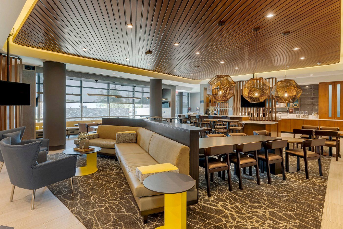 A modern, well-lit lounge area with comfortable seating, dining tables, and stylish light fixtures. The room has a contemporary design and ample space.