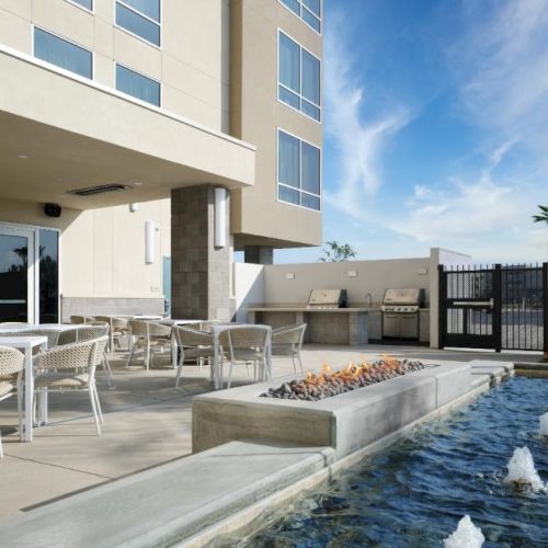 A modern hotel courtyard with a seating area, outdoor dining, and a rectangular pool featuring small fountain jets along the edge.