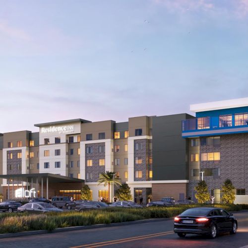 A modern Residence Inn by Marriott hotel with a blue balcony, parking lot, and cars on a dusky evening road.