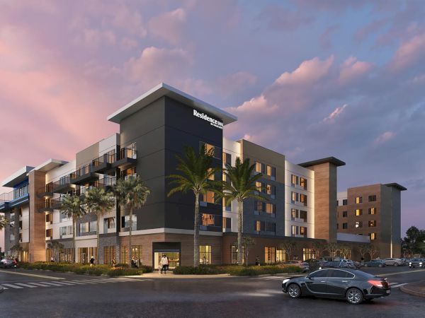 A modern apartment/hotel complex with balconies and palm trees at dusk, labeled &ldquo;Residence Inn,&rdquo; with cars in a parking lot.