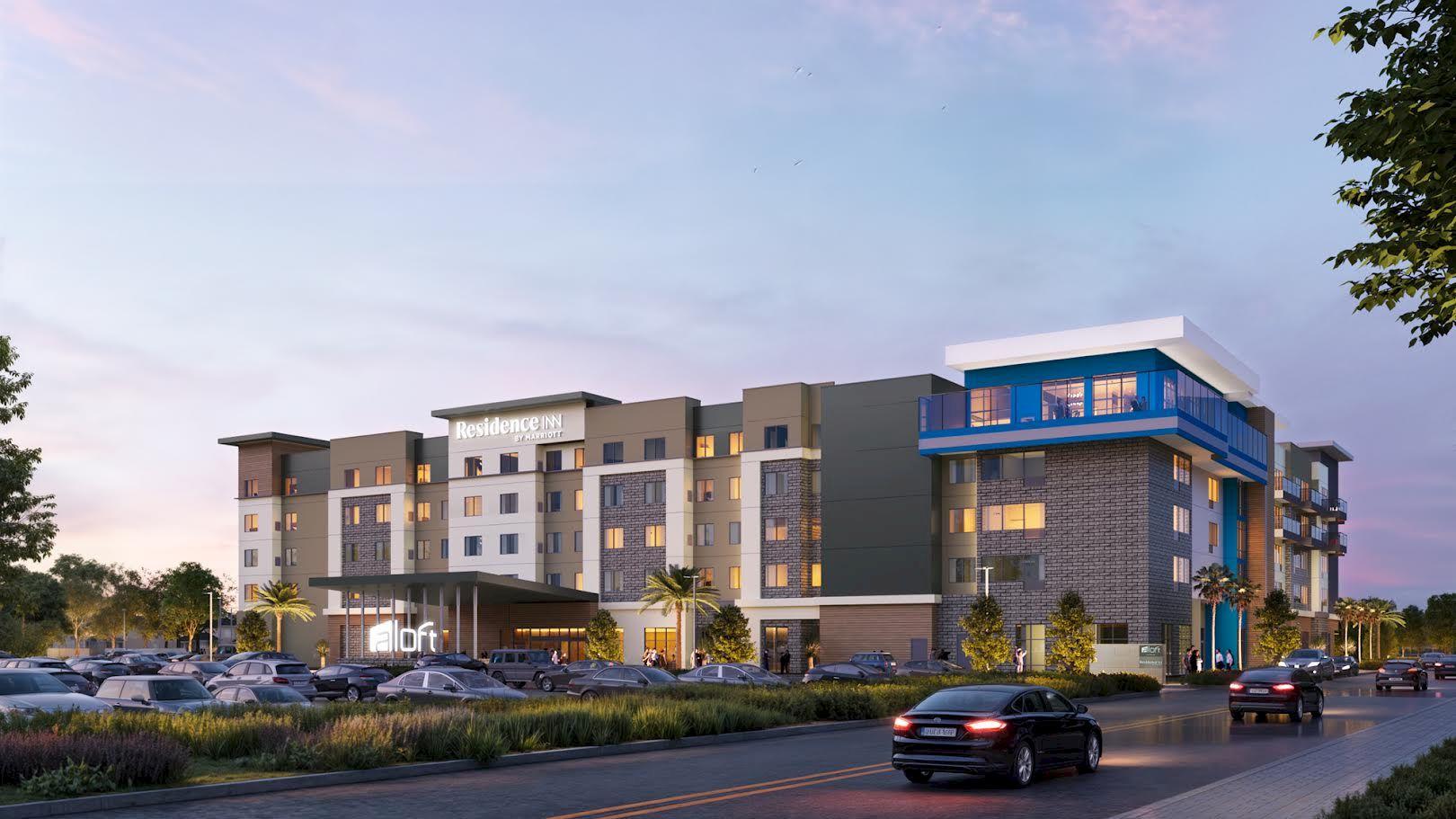 A Residence Inn by Marriott hotel building at dusk, with a busy parking lot and cars along the driveway.