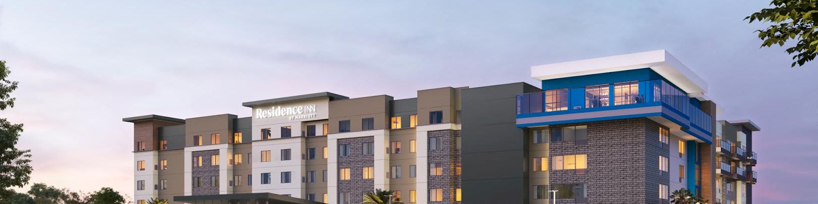 A Residence Inn by Marriott hotel building at dusk, with a busy parking lot and cars along the driveway.