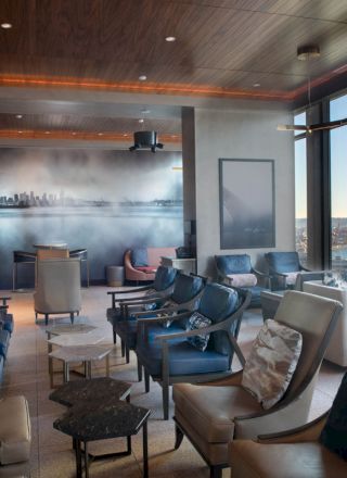 A modern lounge with cushioned seats, a wall mural, and large windows offering a scenic coastal view, including a Ferris wheel, under relaxed lighting.
