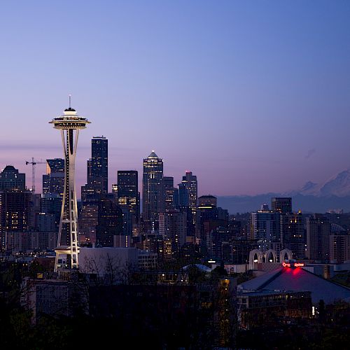 The image shows the Seattle city skyline at dusk, with the Space Needle prominently in view and Mount Rainier visible in the background.