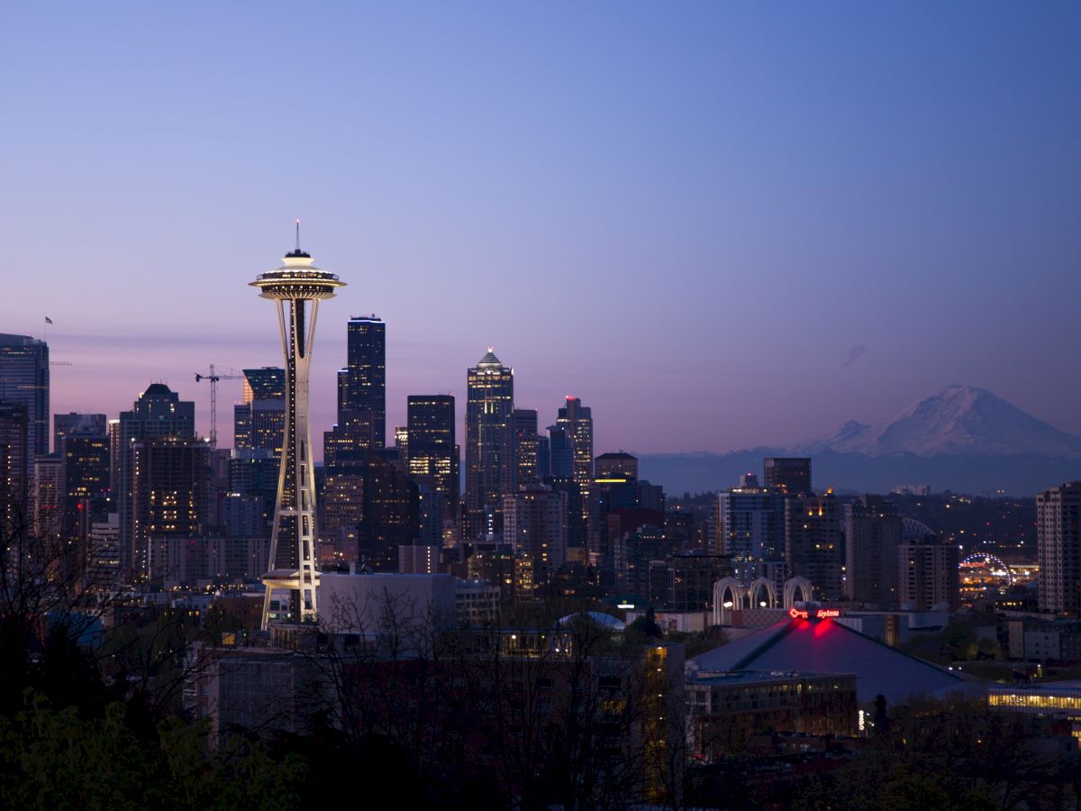 This image shows the Seattle skyline during dusk, including the iconic Space Needle and Mt. Rainier in the background with the sky transitioning to night.